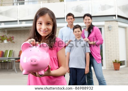 Beautiful little girl inserting coin in a piggy bank with her family in background