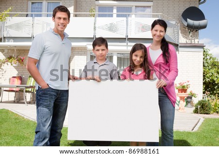 Portrait of young family holding a black white board outside their house