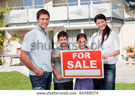 Portrait of family holding for sale sign standing outside their house