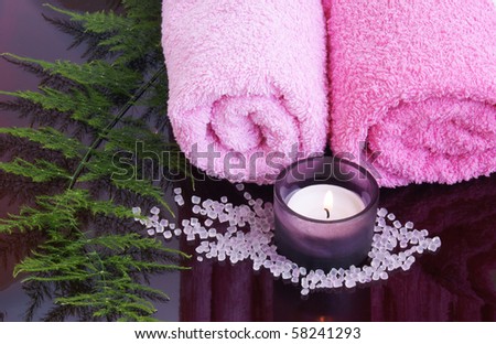 Tranquil spa scene with pink towels, lighted candle, bath salts and plant