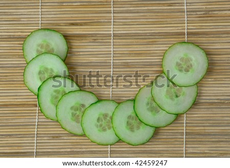 Green pieces of cucumber in half circle shape on bamboo mat