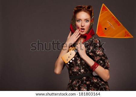 Girl in Russian style posing in red kerchief and bagels on the neck. Holding a balalaika.