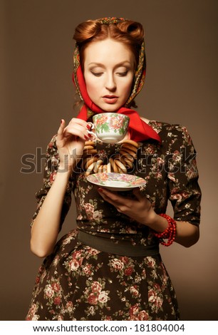 Girl in Russian style posing in red kerchief and bagels on the neck.  Drinking tea from a china cup.