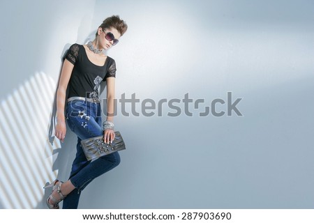 fashion shot of girl with sunglasses holding purse posing in light background