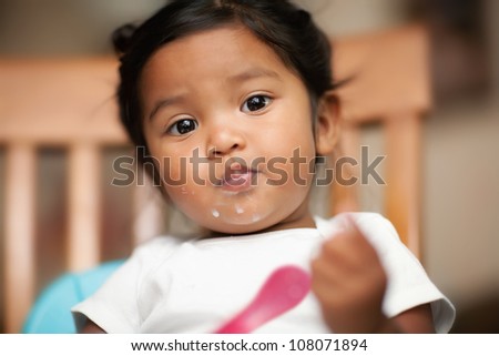 Hispanic baby girl learning to eat by herself with milk spilled on her mouth