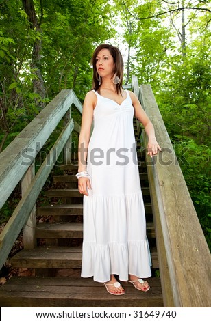 Beautiful Woman in a White Dress Standing on Wooden Steps in the Forest