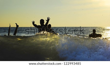 Silhouettes of young group of people jumping in ocean at sunset