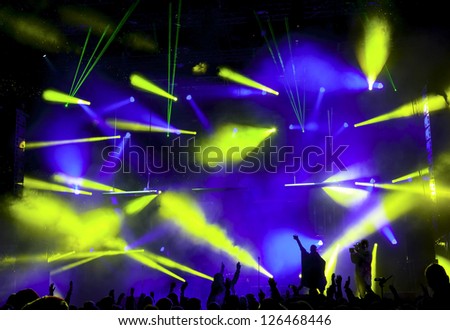 Silhouettes of people and musicians in big concert stage. Bright beautiful rays of light