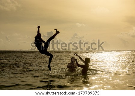 Silhouette of young girl jumping out of the ocean, which throws strong two man on the background of the expiring sunset. Single shooting