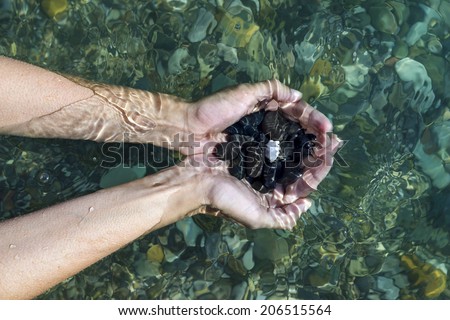 Women\'s hands with a handful of sea stones under water, holds in the clear sea water. Top view