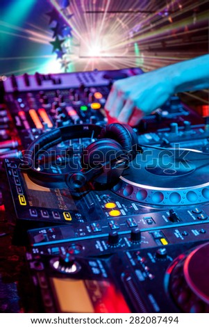 Dj mixes the track in the nightclub at party. In the background laser light show.  Headphones in foreground and DJ hands in motion