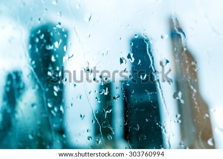 Silhouettes of big towers of the business center behind the wet glass, where on the street cloudy and rain