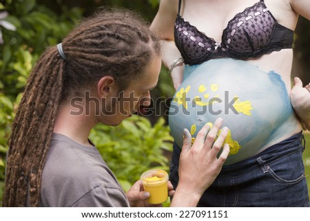 Young Man finger painting on a woman\'s pregnant belly - Germany, Europe