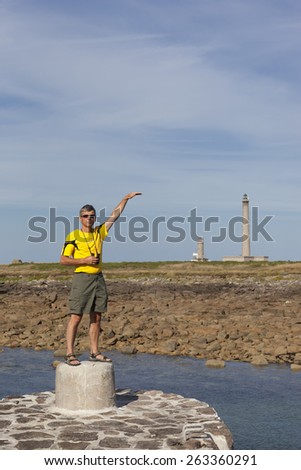 BARFLEUR, FRANCE - JULY 1, 2011: Mature man standing on granite block and holding hand to the height of a lighthouse. This lighthouse is the third tallest traditional lighthouse in the world.