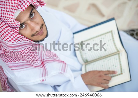 Young Arabic Muslim man reading Koran and praying