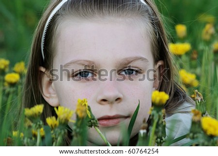 Portrait of nice, young girl in the dandelion meadow on summer day.
