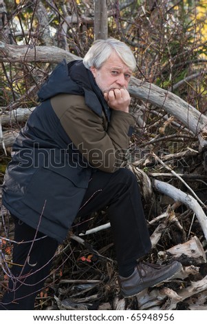 Mature serious man with grey hair in forest in autumn day.