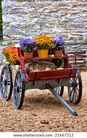 Old horse drawn wagon filled with flowers and pumpkins against old stone wall