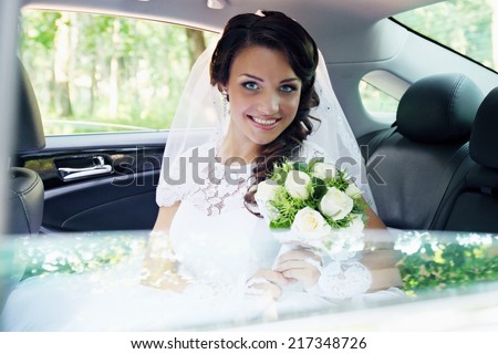 beautiful bride with a bouquet of roses sitting in the car