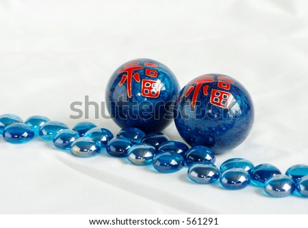 Two blue metal Happiness Balls, stand next to a stream of blue beads.