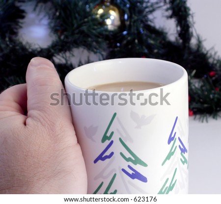 Hand holds Christmas mug with tree decoration in background.