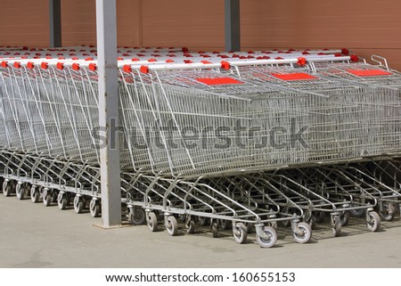 A lot of Shopping trolleys on wheels made of metal, for products and goods stand in a row near the shop