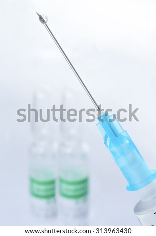 Medical syringe with a droplet of fluid injection, large, close-up. Medical ampoules in the background is blurred