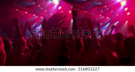 A crowd of spectators at a concert applauded their hands up. People in the red ramps. The blurred image for the background