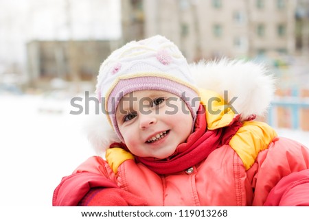 Beautiful happy kid in the red jacket in the winter outdoors.