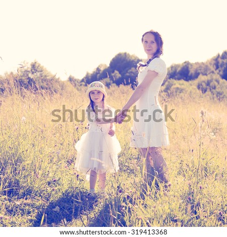 Mother and daughter walking on the sunny meadow.