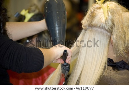 at the hair salon, a blond woman is having her hair styled with brush and hairdryer