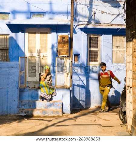 Jodhpur, India - 2015, January 3 : An old rajasthani woman sitting on a porch and a kid in school uniform walking at dawn on the street in the old blue city of Jodphur, Rajasthan, India