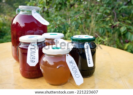 homemade compote and jam pots with Russian labels on the table on orchard background
