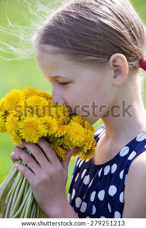 young caucasian girl smelling a bunch of yellow dandelions in hands on green grass background