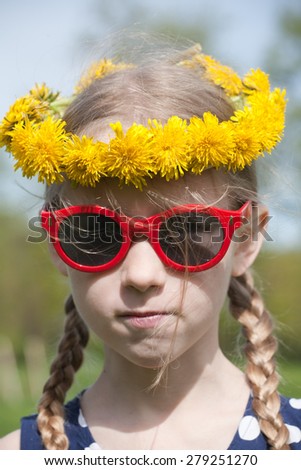 funny young pretty caucasian girl face in yellow dandelions garland on the head and red sunglasses