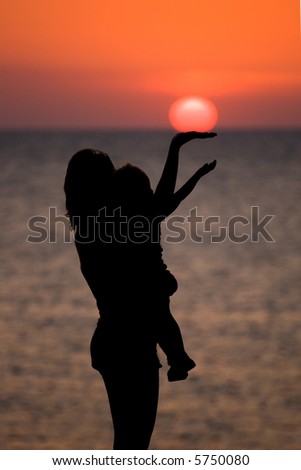 silhouette of woman and child on her hands with sun on palm on sunset sea background