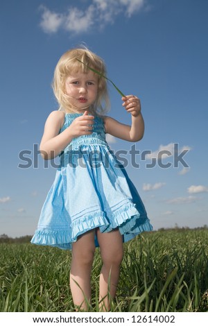 funny little girl with blade of grass in hands on green summer meadow