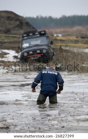 Russian rescuer stand in cold water near to  got stuck car