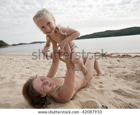 Mum with daughter play on beach, mum lies on sand and holds a daughter upward