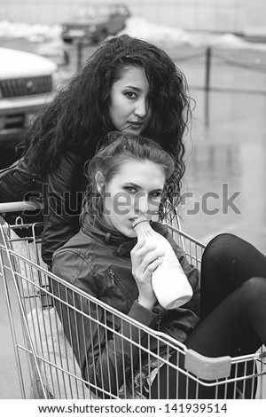 Happy three naughty women with shopping cart. Drink milk outdoors. Effect of the scanned black-and-white film