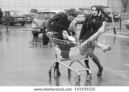 Happy three naughty women with shopping cart. Drink milk outdoors. Effect of the scanned black-and-white film