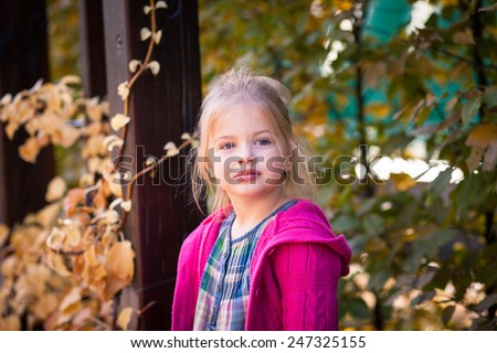 smiling funny little girl in bright clothes. It is baby girl with blue eyes and blond hair. She dresses on clothes with pink blue and green colors. Background is diffused with orange green and brown