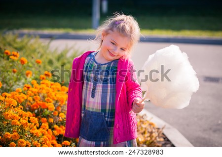 Pretty little girl with shy smile in bright clothes with candyfloss near the bright colored autumn flowers