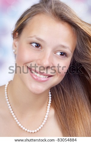The beautiful girl pleasantly smiles in pearls and a flying hair.