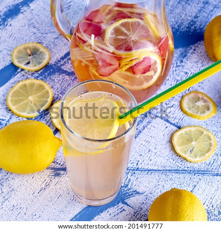 Fresh and cold ginger lemonade with strawberry in glass with pitcher and lemons around it