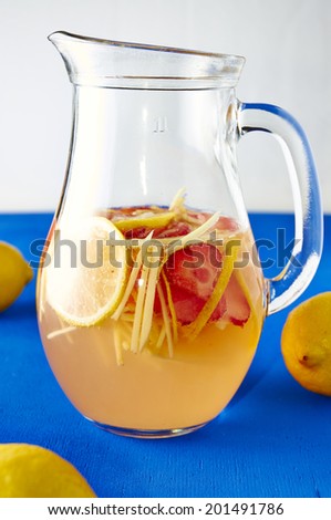 Fresh ginger lemonade with strawberry in pithcer on blue background with lemons around it.