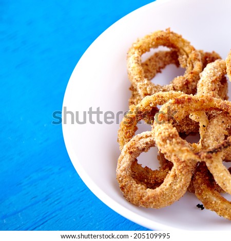 Baked onion rings snacks in white plate on blue background. Healthy fast food recipe.
