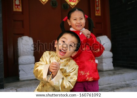 Two children(5-24 years) standing in front of chinese traditional house door smiling