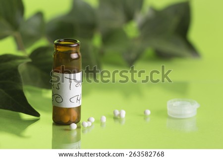 bottle of homeopathic medicine with globules, background with ivy