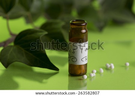 bottle of homeopathic medicine with globules, background with ivy